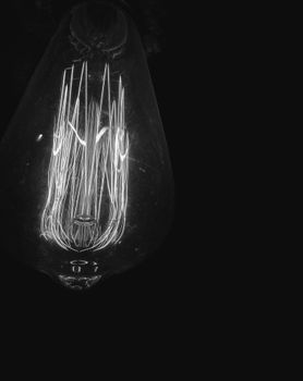 Grayscale close-up of an illuminated light bulb showcasing intricate filament details.