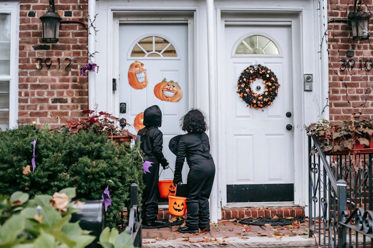 Anonymous Kids In Halloween Costumes Standing On Porch With Buckets