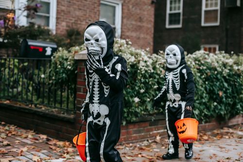 Free Faceless kids in black skeleton costumes in masks with orange buckets in Halloween walking on street in day Stock Photo