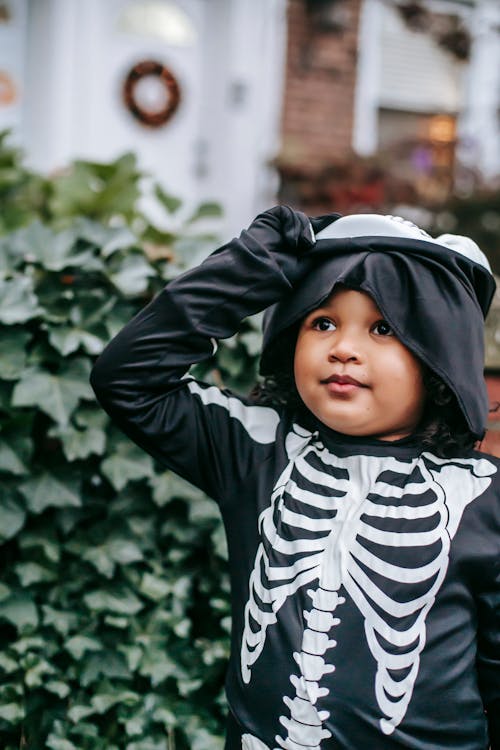 Kid in skeleton costume standing outside in Halloween