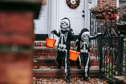 Free Full body of faceless children in black skeleton costumes with masks and buckets in Halloween walking down on stairs near house door in day Stock Photo
