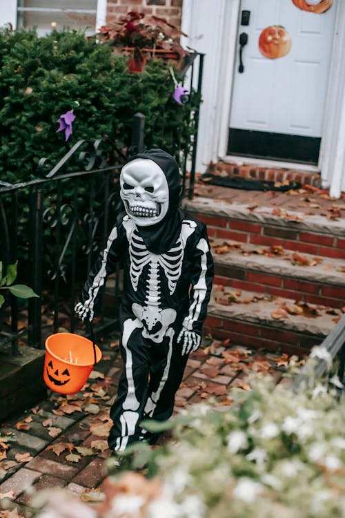 Full length of unrecognizable child in skeleton costume with mask and bucket trick or treating in Halloween