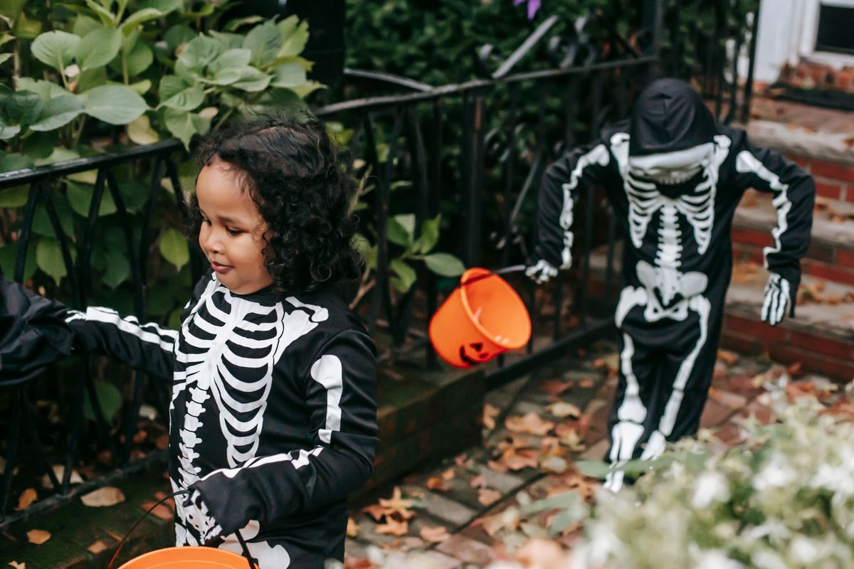 Children trick-or-treating outdoors in skeleton costumes.