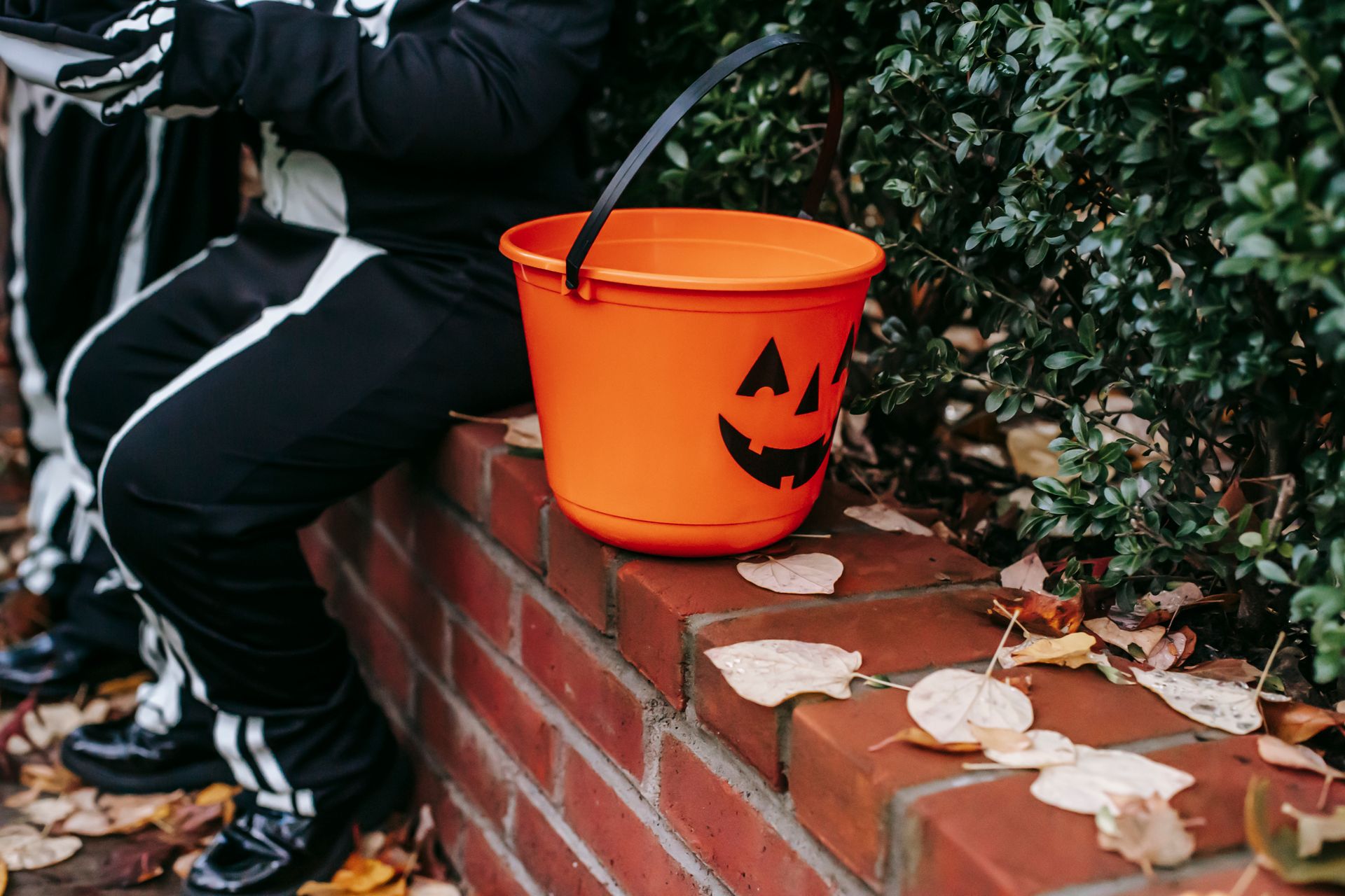 Crop child sitting with plastic bucket decorated as jack o lantern