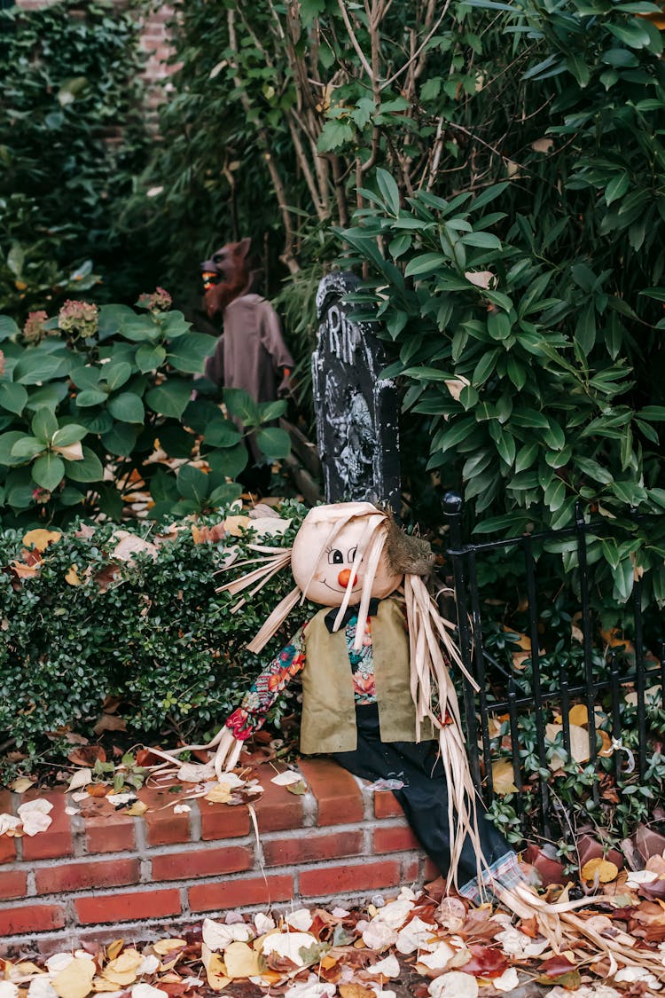 Scarecrow Located On Brick Fence Of Garden On Autumn Day