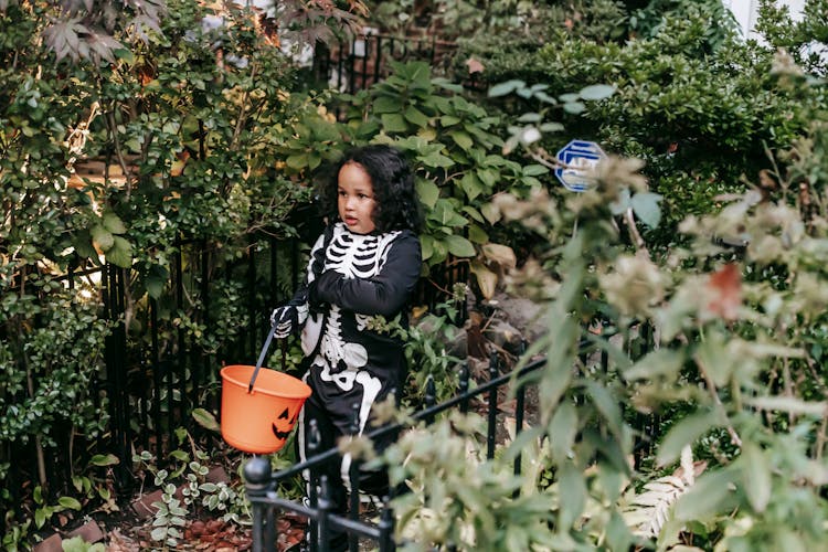 Curious Black Girl In Costume Standing With Bucket Before Trick Or Treat