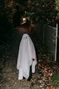 Anonymous child in scary ghost costume standing in empty dark pathway between gardens and looking at camera