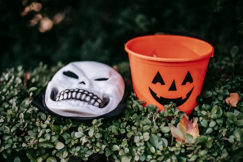 Spooky skeleton mask placed near orange bucket outdoors
