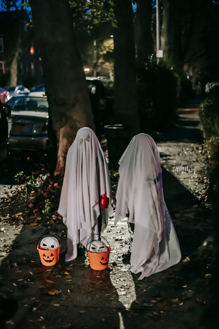 Orange Buckets With Masks Placed Near Children In Halloween Costumes At Night