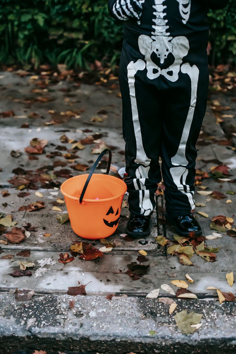 Crop Little Kid In Skeleton Costume Trick Or Treating With Orange Bucket