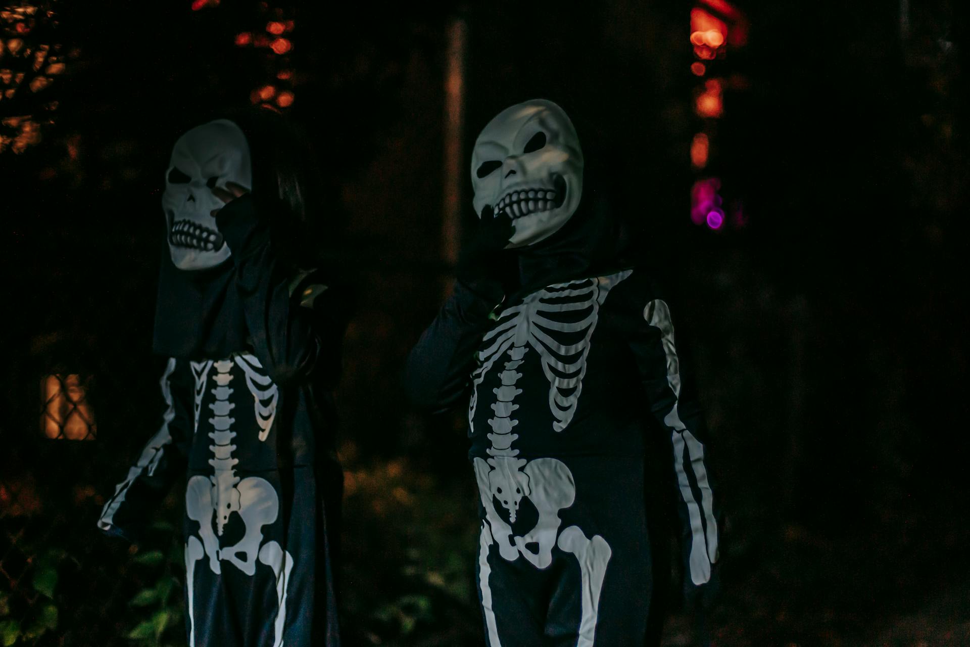 Unrecognizable persons dressed in costumes of skeleton standing on dark street