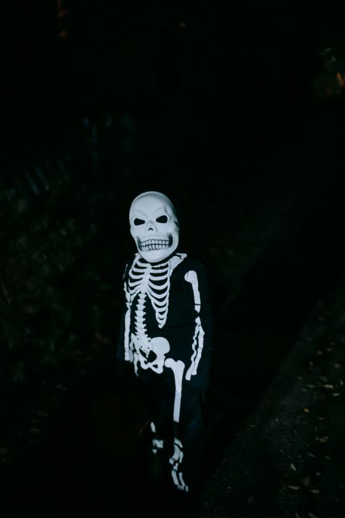 Free Full body of confident anonymous kid in skeleton costume and skull mask standing in dark park and looking at camera while Halloween Stock Photo