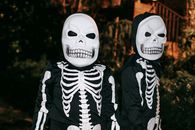 Creepy unrecognizable persons in skeleton costumes and skull masks standing together on dark street at night time during Halloween celebration