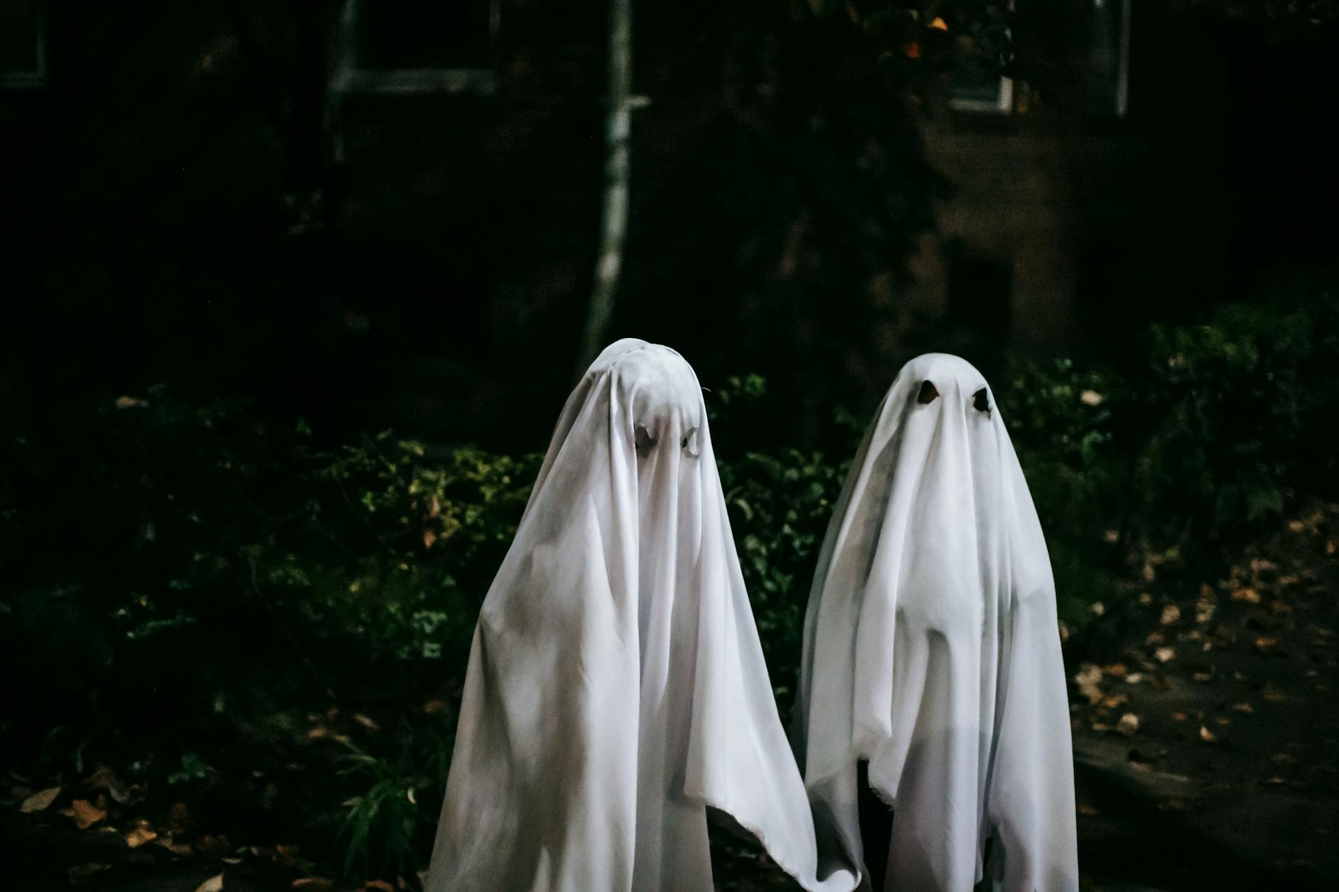 Anonymous friends in phantom costumes with holes for eyes spending time together on Halloween night in city