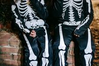 Crop anonymous kids in costumes with skeleton print resting during festive event in autumn at dusk