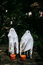 Unrecognizable kids in ghost costumes with plastic buckets in form of carved pumpkins celebrating festive event in night city