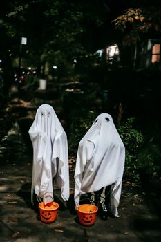 在夜城庆祝节日的孩子们穿着幽灵服装，提着用塑料桶雕刻的南瓜灯