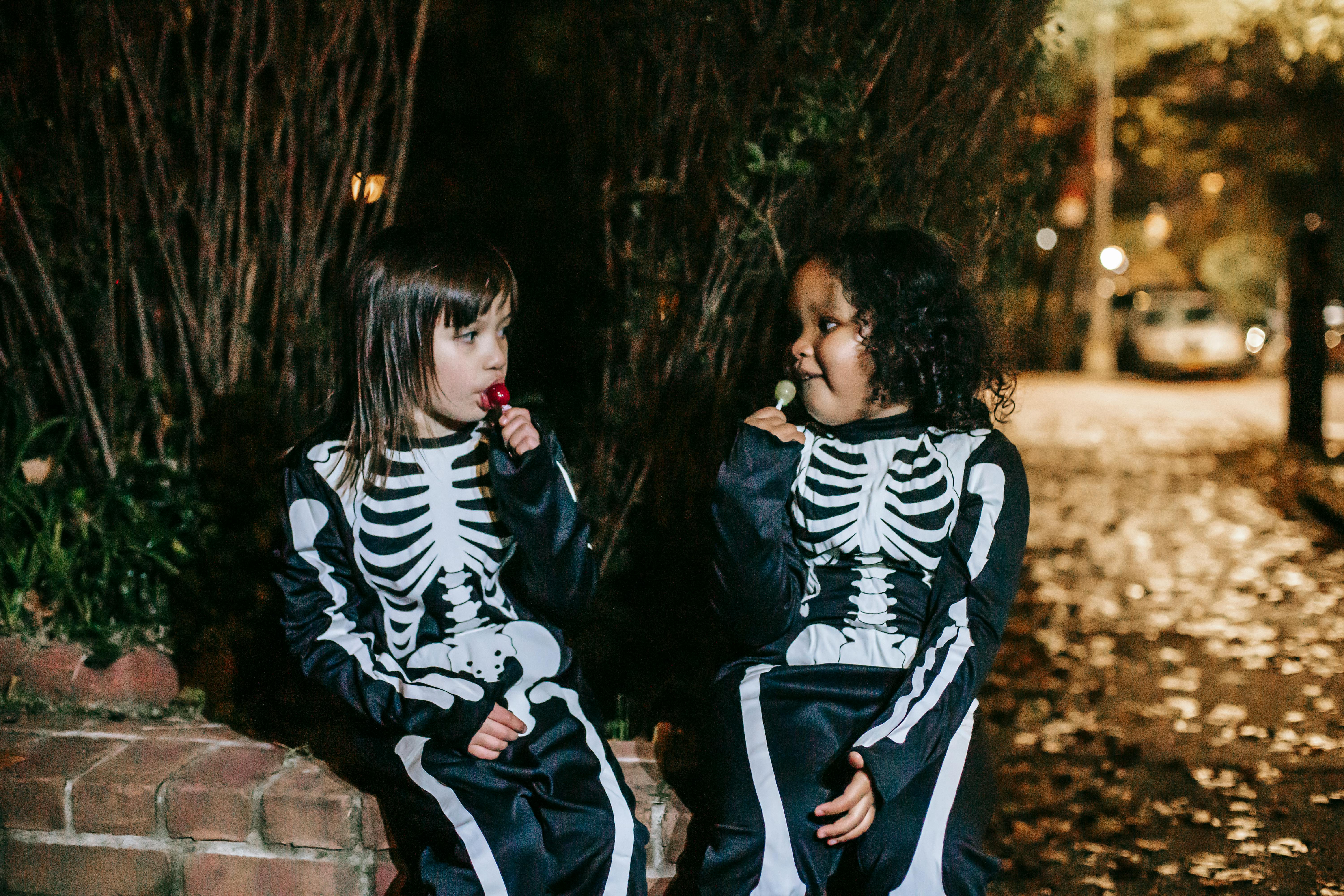 multiethnic girlfriends eating tasty lollipops in park on halloween night