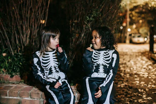 Multiethnic girlfriends eating tasty lollipops in park on Halloween night