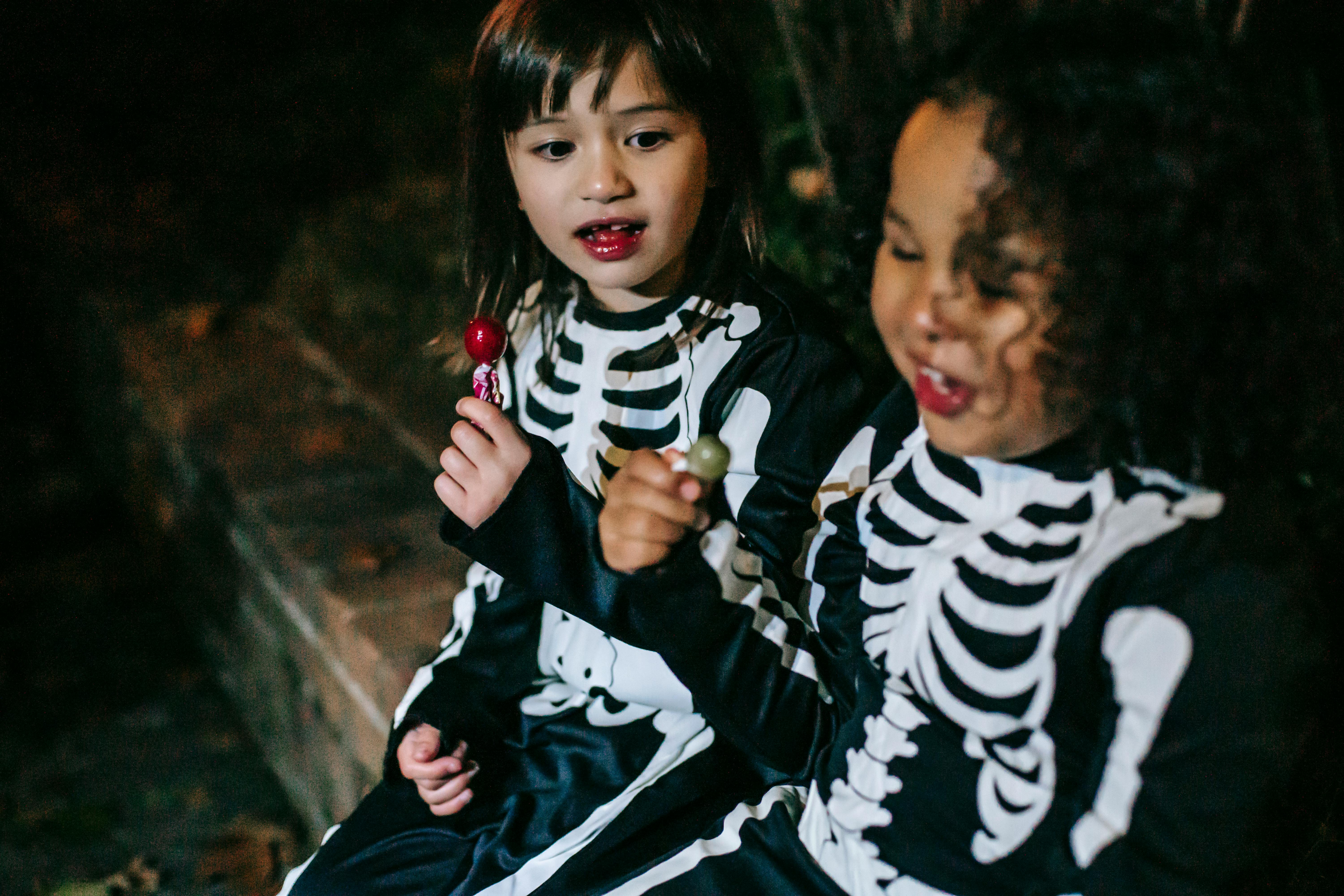 crop happy diverse girls in skeleton costumes enjoying stick candies