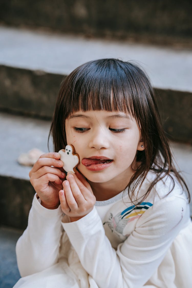 Adorable Ethnic Girl Holding Traditional Ghost Cookie Near Pretty Face