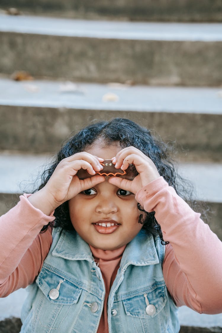 Cheerful Ethnic Girl Holding Spooky Bat Cookie Near Face