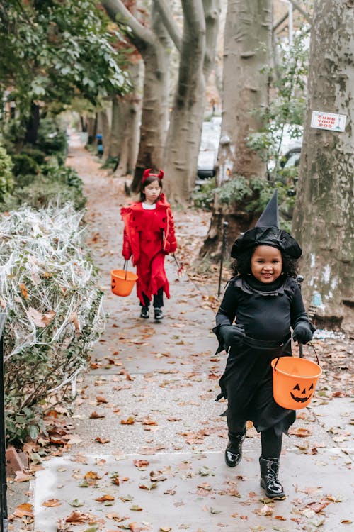 Cheerful cute girls in Halloween costumes walking in autumn park