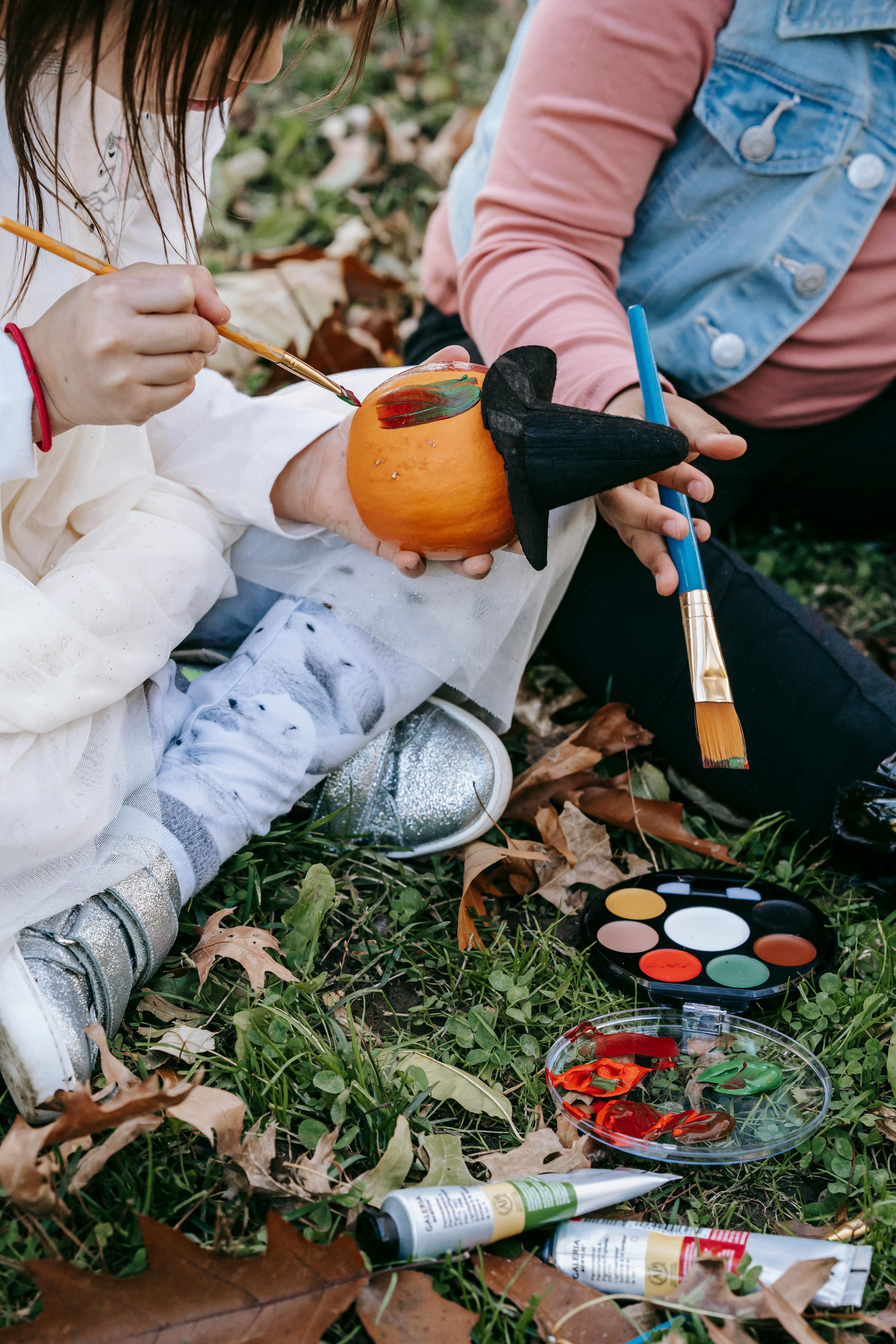 crop faceless girls painting halloween pumpkin in park