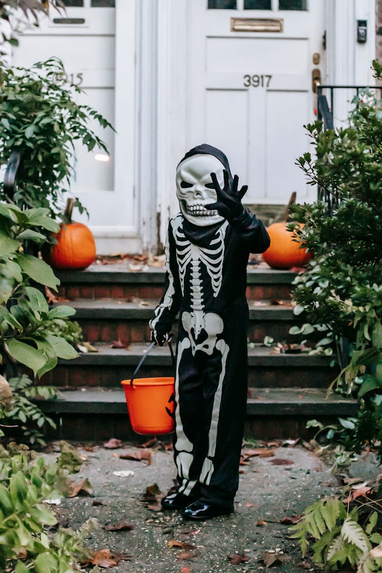 Unrecognizable Child In Halloween Costume Standing With Bucket In Street