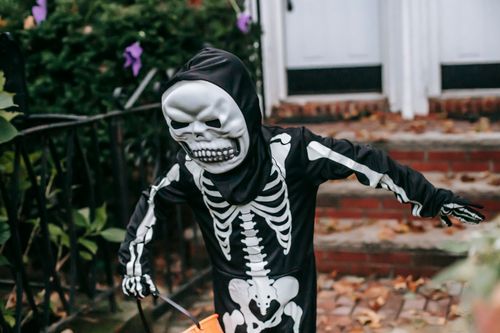 Free Anonymous kid with bucket wearing skeleton costume and mask walking on terrace of building after trick or treat game during Halloween celebration Stock Photo