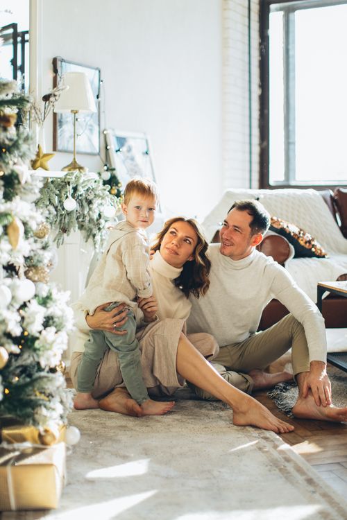 Free A family of three enjoying festive moments by the Christmas tree indoors. Stock Photo