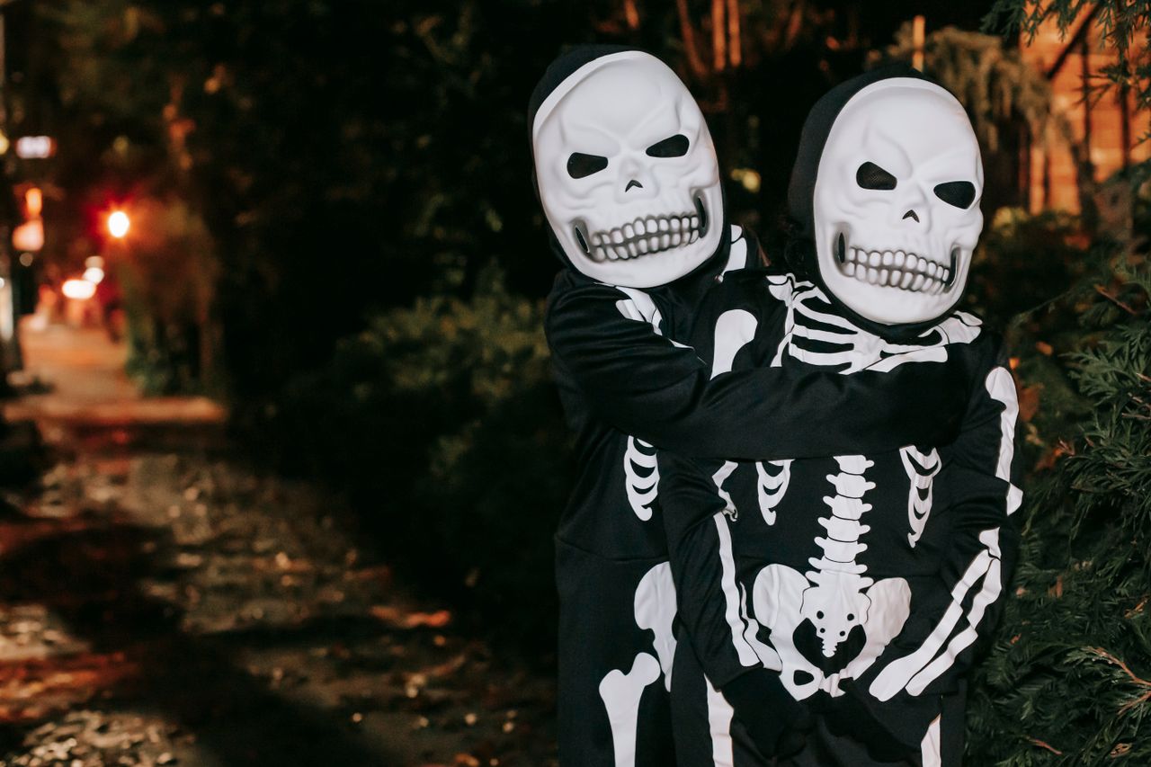 anonymous kids in skeleton costumes and masks embracing while standing