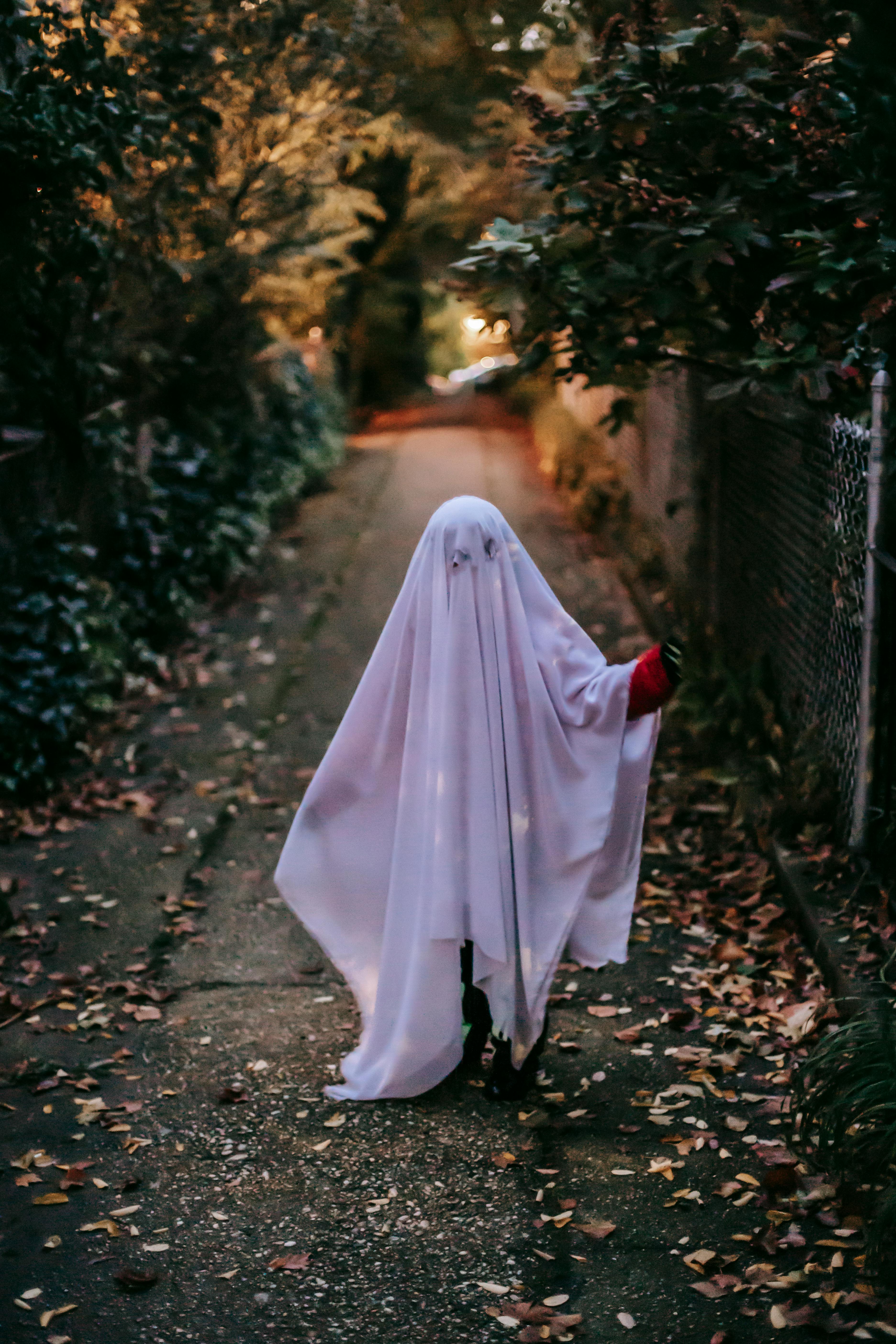 unrecognizable kid in ghost costume walking on walkway