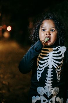 万圣节之夜，年幼的孩子穿着骷髅服装在户外吃棒棒糖