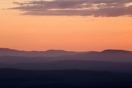Scenic view of layered mountains under a vibrant sunset sky, capturing nature's tranquility.