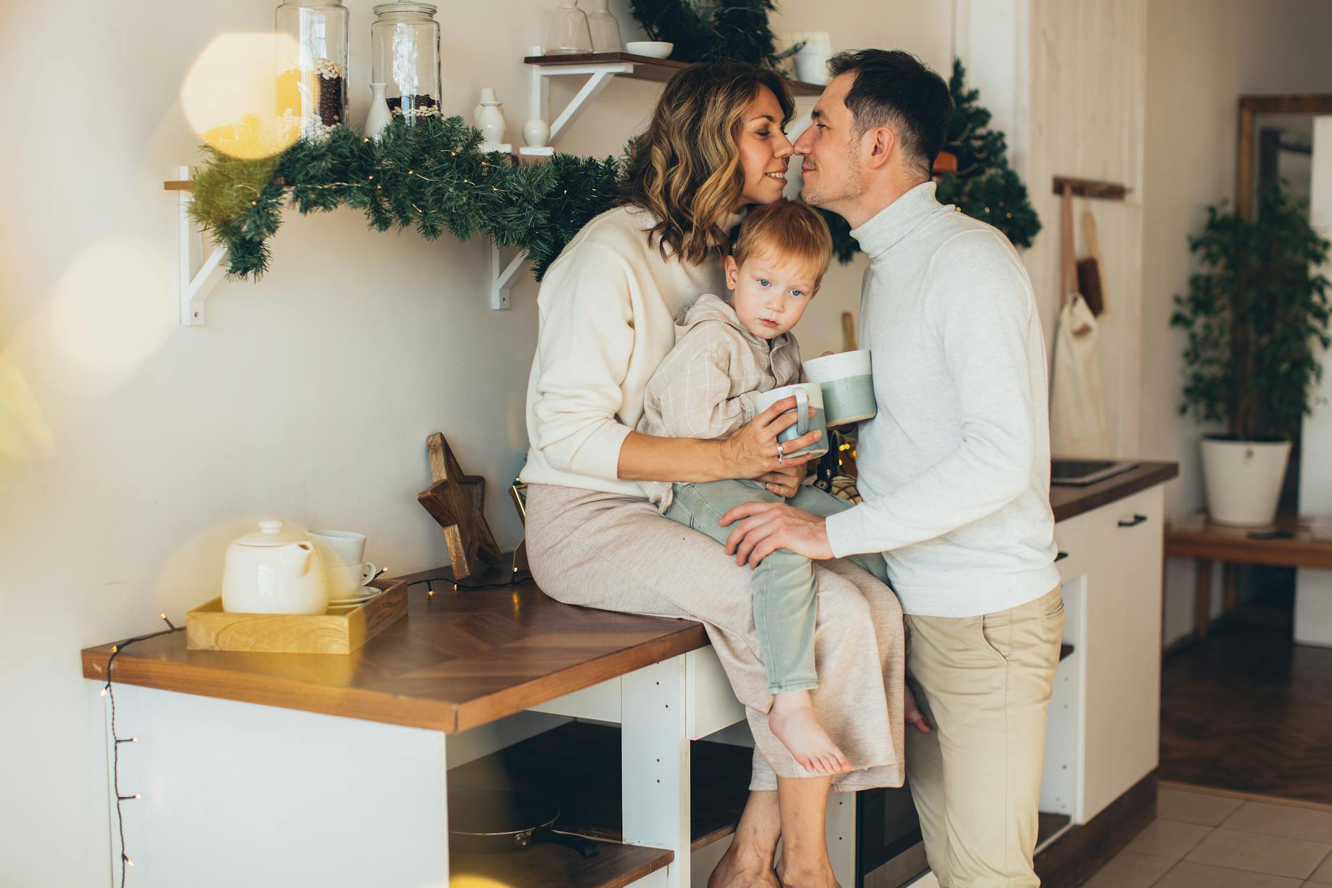 A family shares a tender moment in a stylish and cozy holiday-themed kitchen.