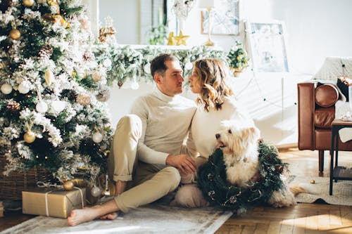 A Couple Sitting next to a Christmas Tree with their Dog