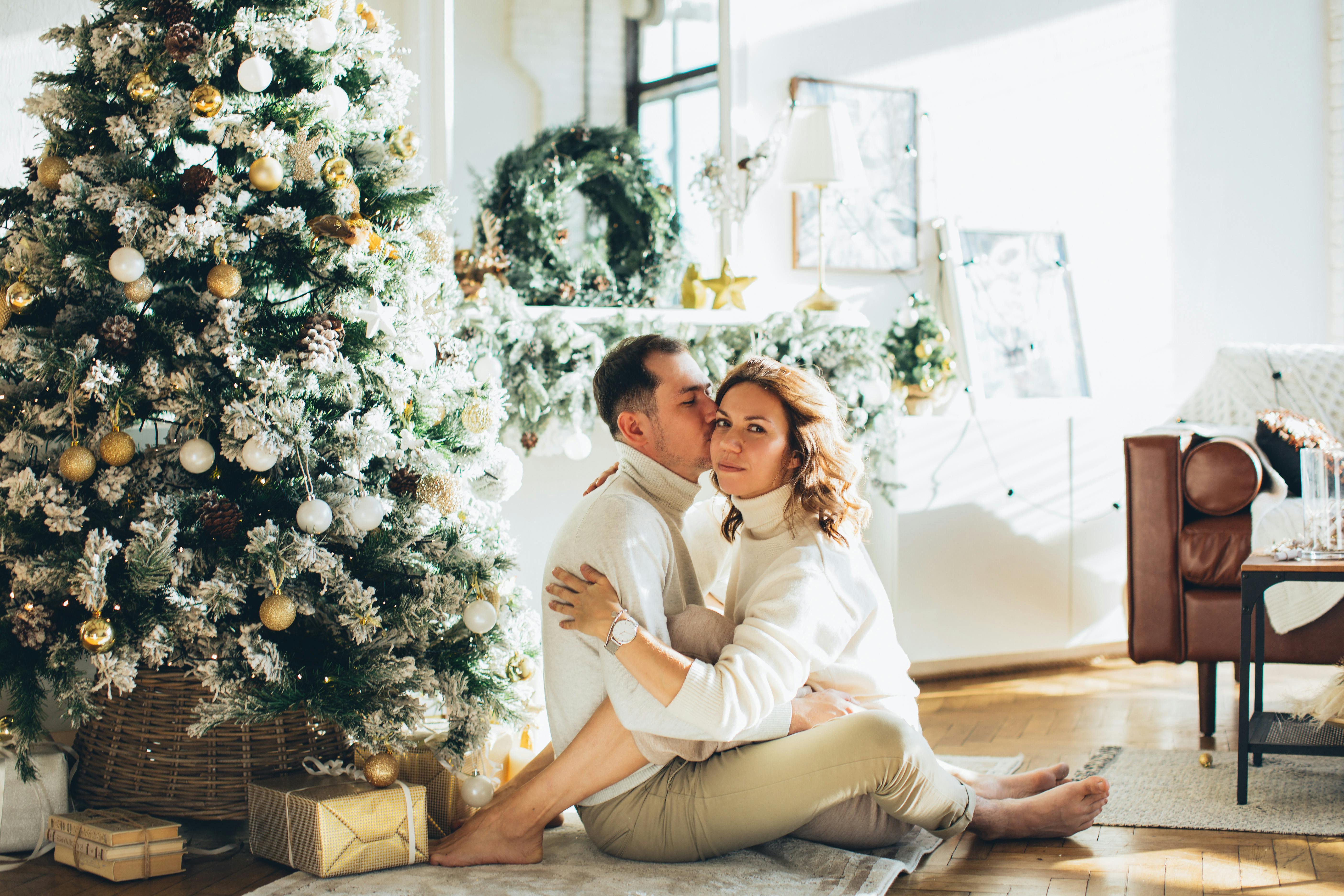 A couple sitting by the Christmas tree in a warmly lit living room, embracing the holiday spirit.