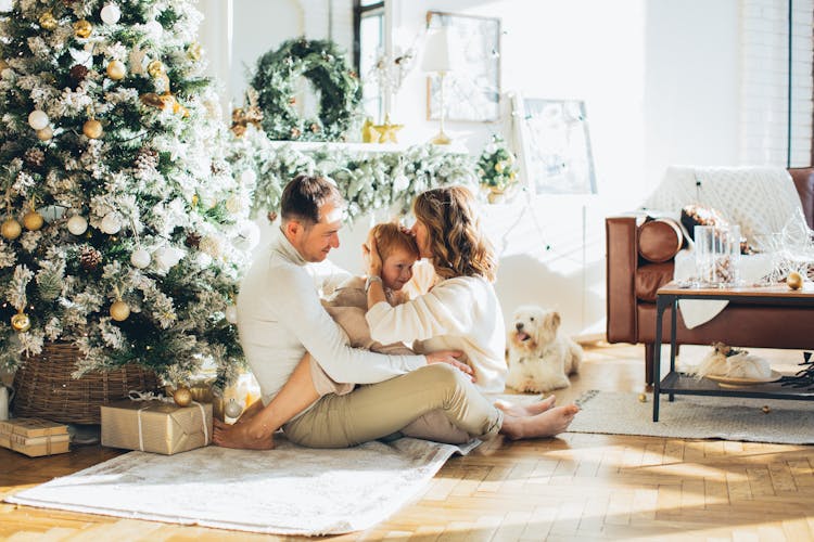 Photo Of A Happy Family Sitting Beside The Christmas Tree With Their Dog