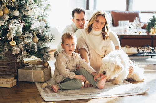 Photo of a Happy Family Sitting Beside the Christmas Tree with Their Dog