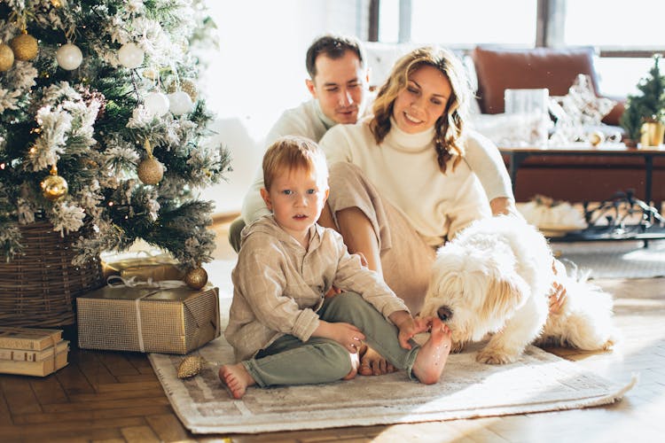 Photo Of A Happy Family Sitting Beside The Christmas Tree With Their Dog