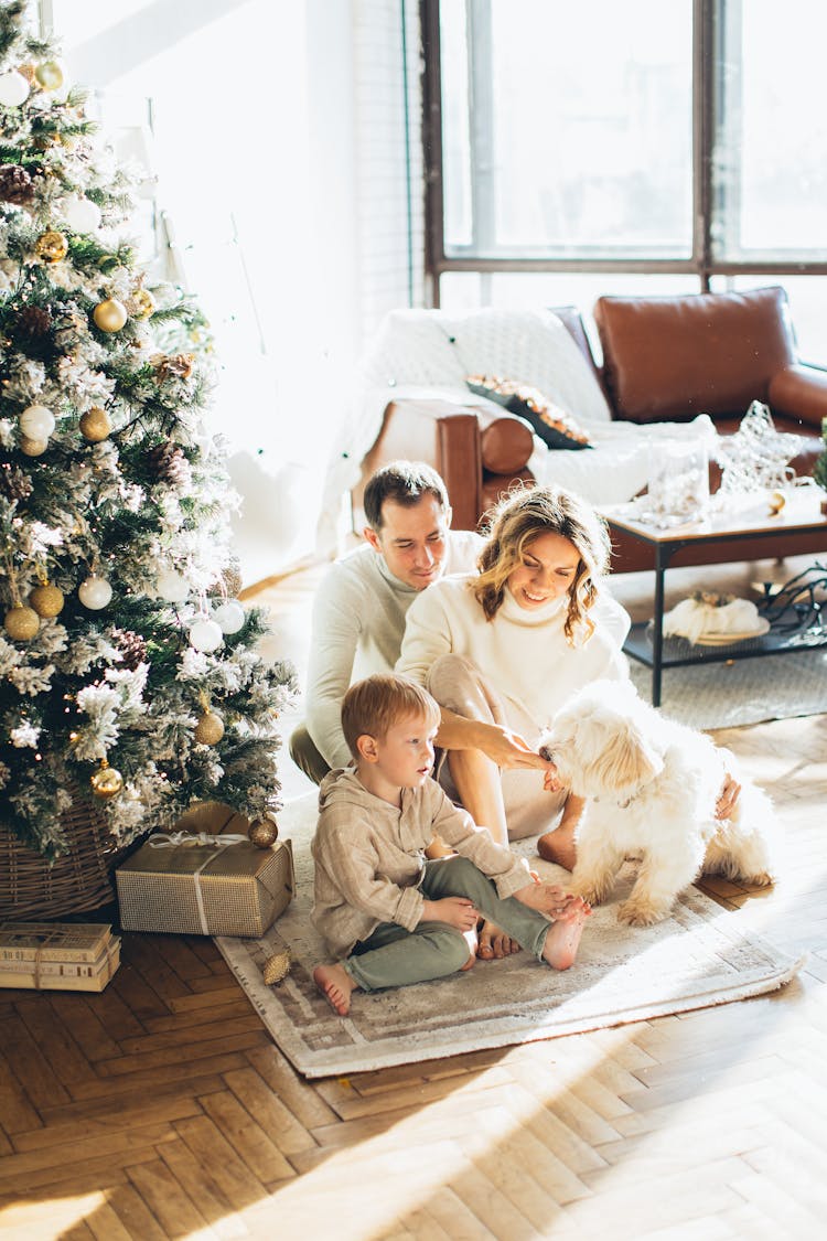 Photo Of A Happy Family Sitting Beside The Christmas Tree With Their Dog