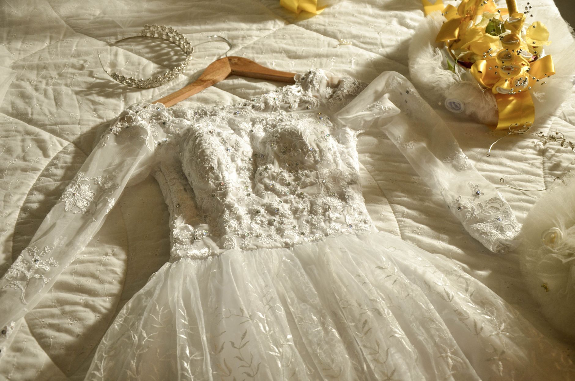 Beautiful lace bridal gown with tiara laid on bed, perfect for wedding themes.