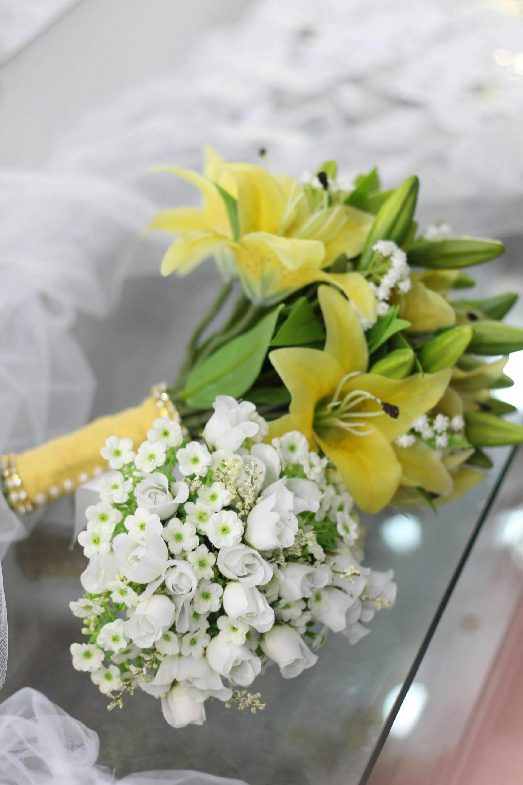Free A close-up of a bridal bouquet featuring yellow lilies and white flowers on a reflective surface. Stock Photo