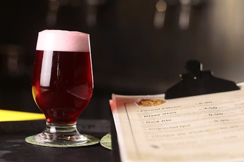 Free Clear Drinking Glass of Red Ale Beside a Menu Stock Photo