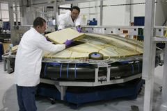 Concentrated male mechanics in protective uniform assembling detail of large spacecraft component at modern factory