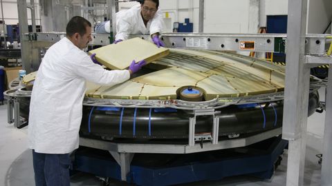 Concentrated male mechanics in protective uniform assembling detail of large spacecraft component at modern factory