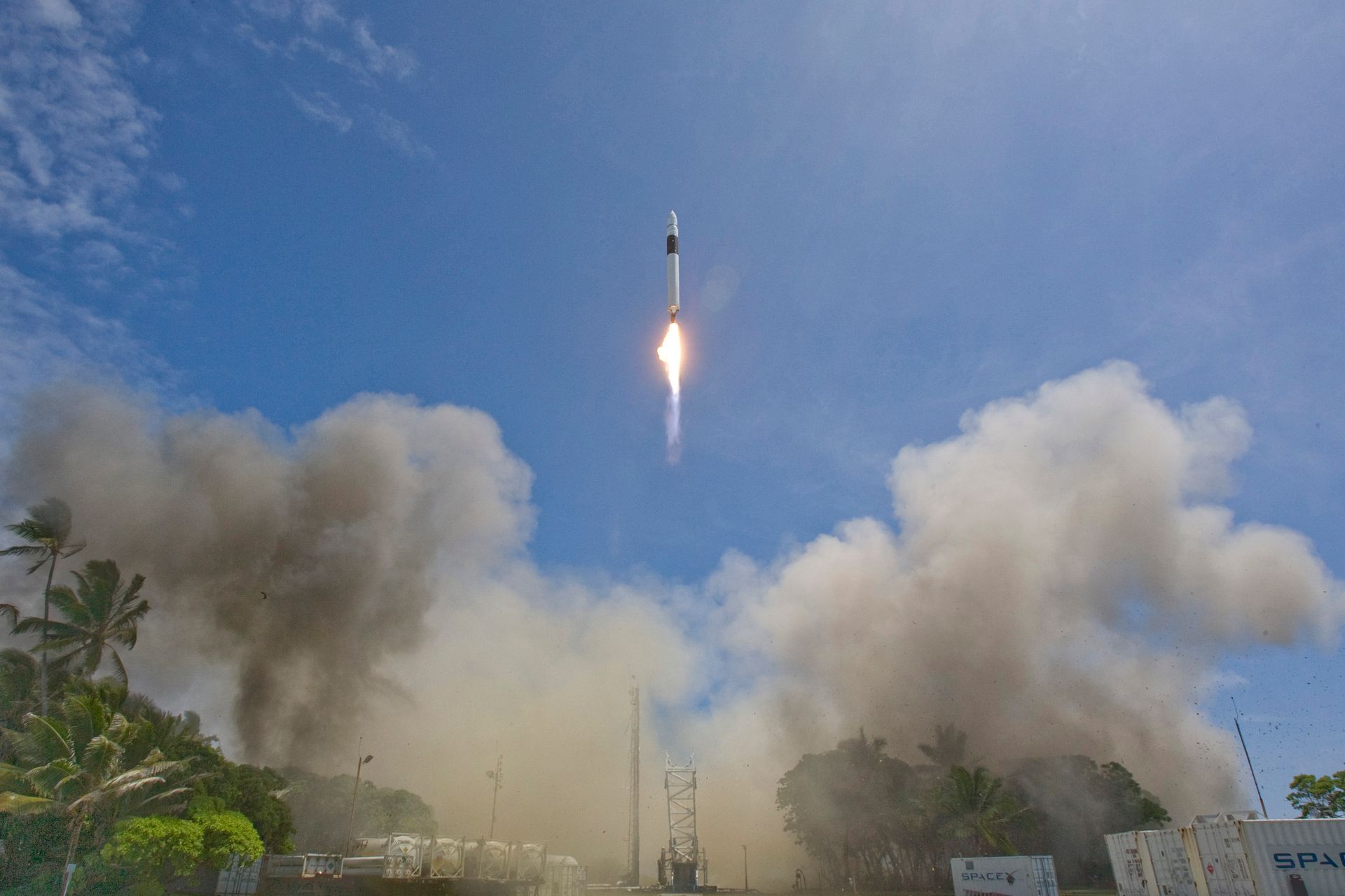 A rocket launches into a clear blue sky, leaving smoke and flames behind.