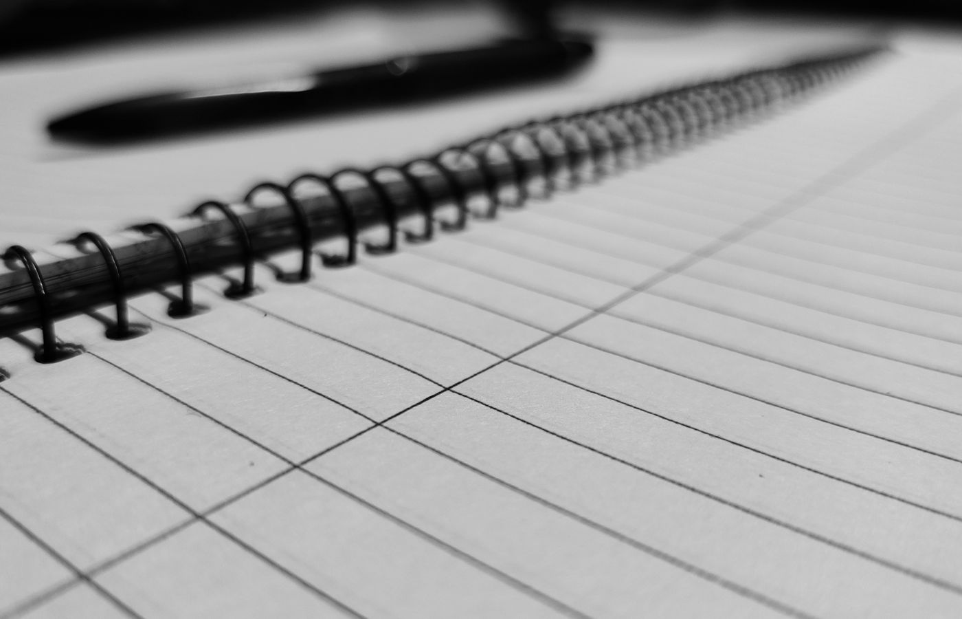 Monochrome close-up of a spiral notebook with pen, highlighting office stationery.