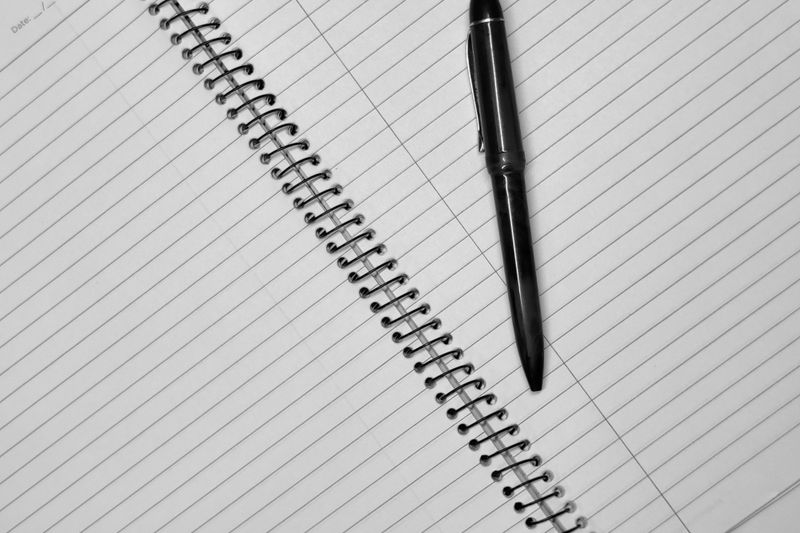 Close-up of a black pen resting on an open spiral notebook with lined pages.
